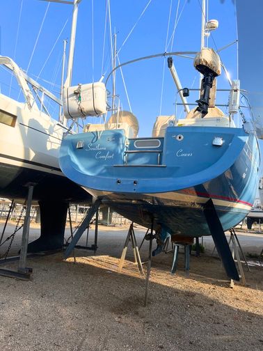 southerly on a stand in the marina, the boat has a dark blue bottom, with a lighter blue coat which would be seen above the surface
